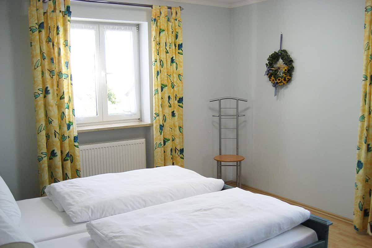 Un dormitorio con dos camas, una ventana con cortinas, un radiador, un estante en la pared y una guirnalda.