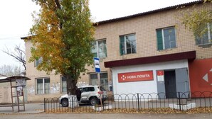 A building with a sign reading "Нова Політика" and a fenced area with a tree and parked cars.