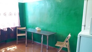 A room with a green wall, a wooden floor, a table with chairs, a small wooden stool, and a white cabinet.