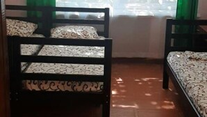 A room with two wooden beds, a window with green curtains, and a wooden floor.