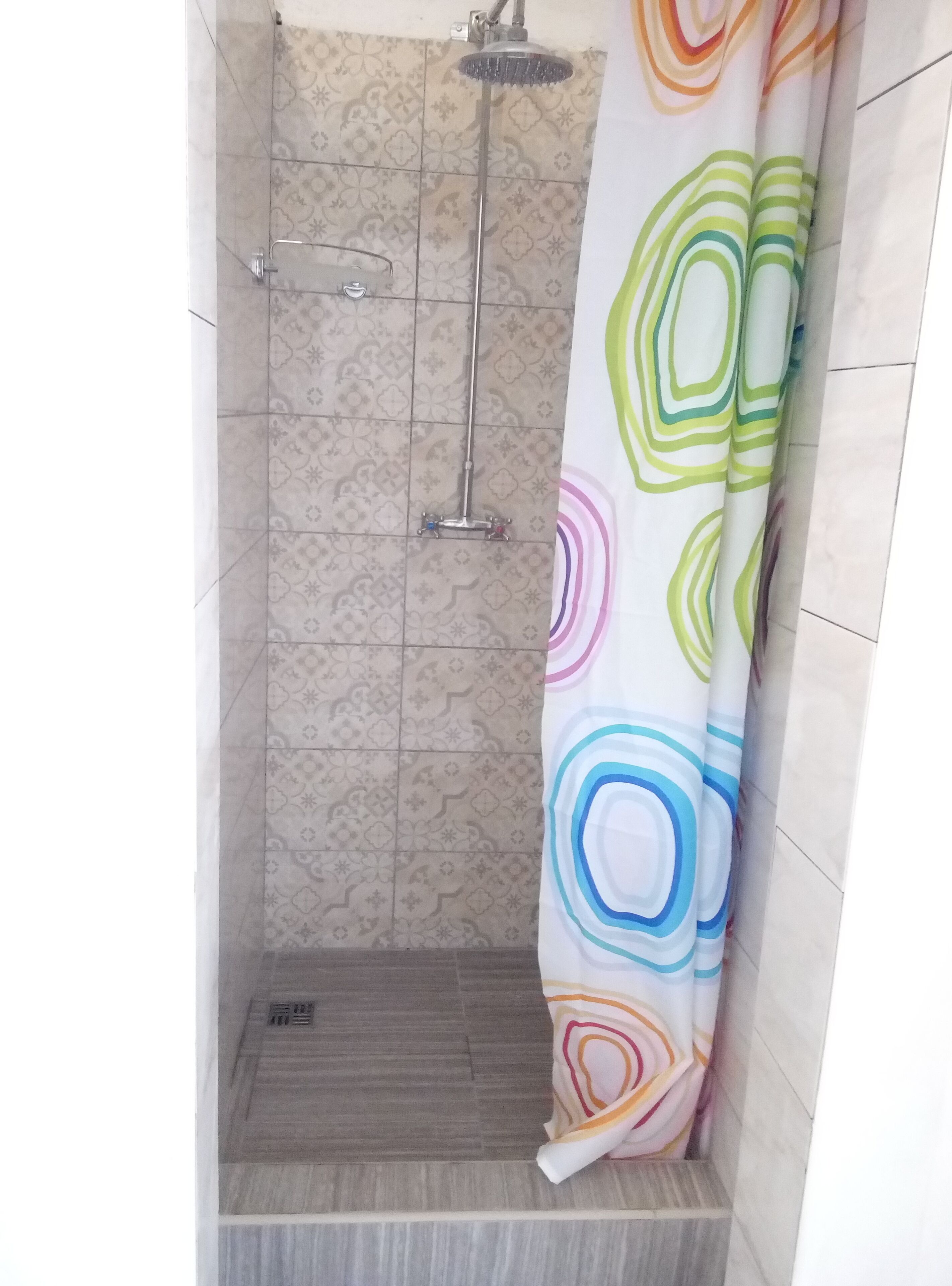A shower area with a patterned tile wall, a showerhead, and a colorful shower curtain.