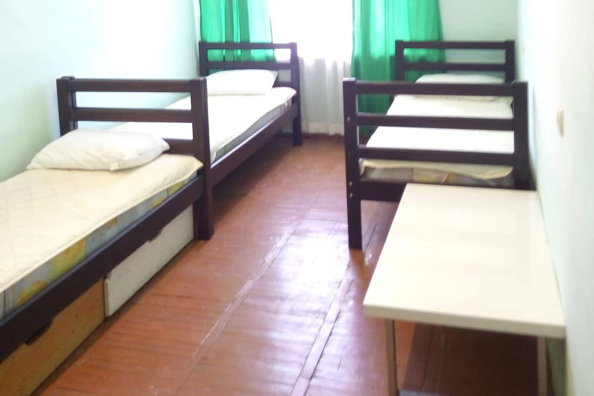 Un dormitorio con dos literas, una mesita pequeña y una ventana con cortinas verdes.