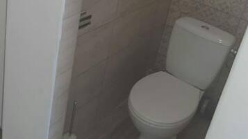 Un baño pequeño y estrecho con inodoro, un dispensador de papel higiénico en la pared y una escoba para el suelo.