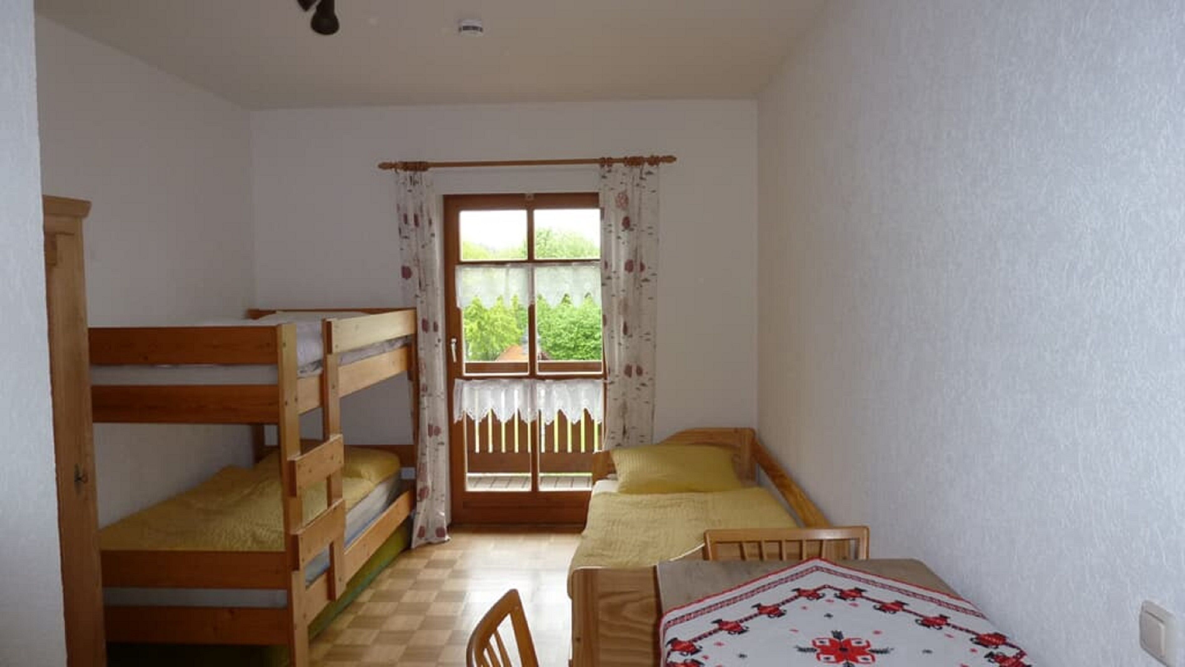 Una habitación con literas, una ventana con cortinas, piso a cuadros y una mesa con mantel.