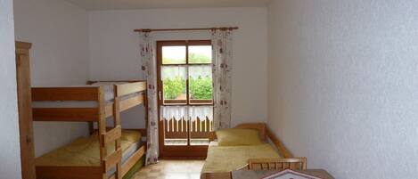 Una habitación con literas, una ventana con cortinas, piso a cuadros y una mesa con mantel.