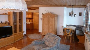 A cozy living room with a television, wooden cabinet, and a patterned armchair. - Appartementhaus Osserblick (Lohberg)
