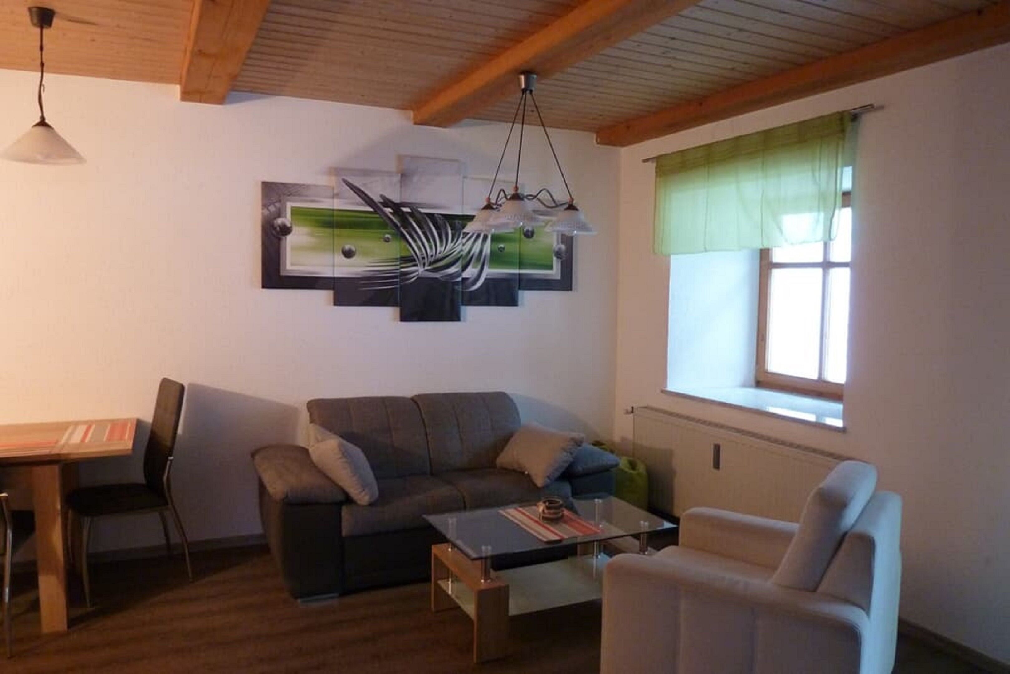 Una sala de estar con un sofá, una mesa de centro, una silla, una mesa de comedor con sillas y una ventana con cortina verde.