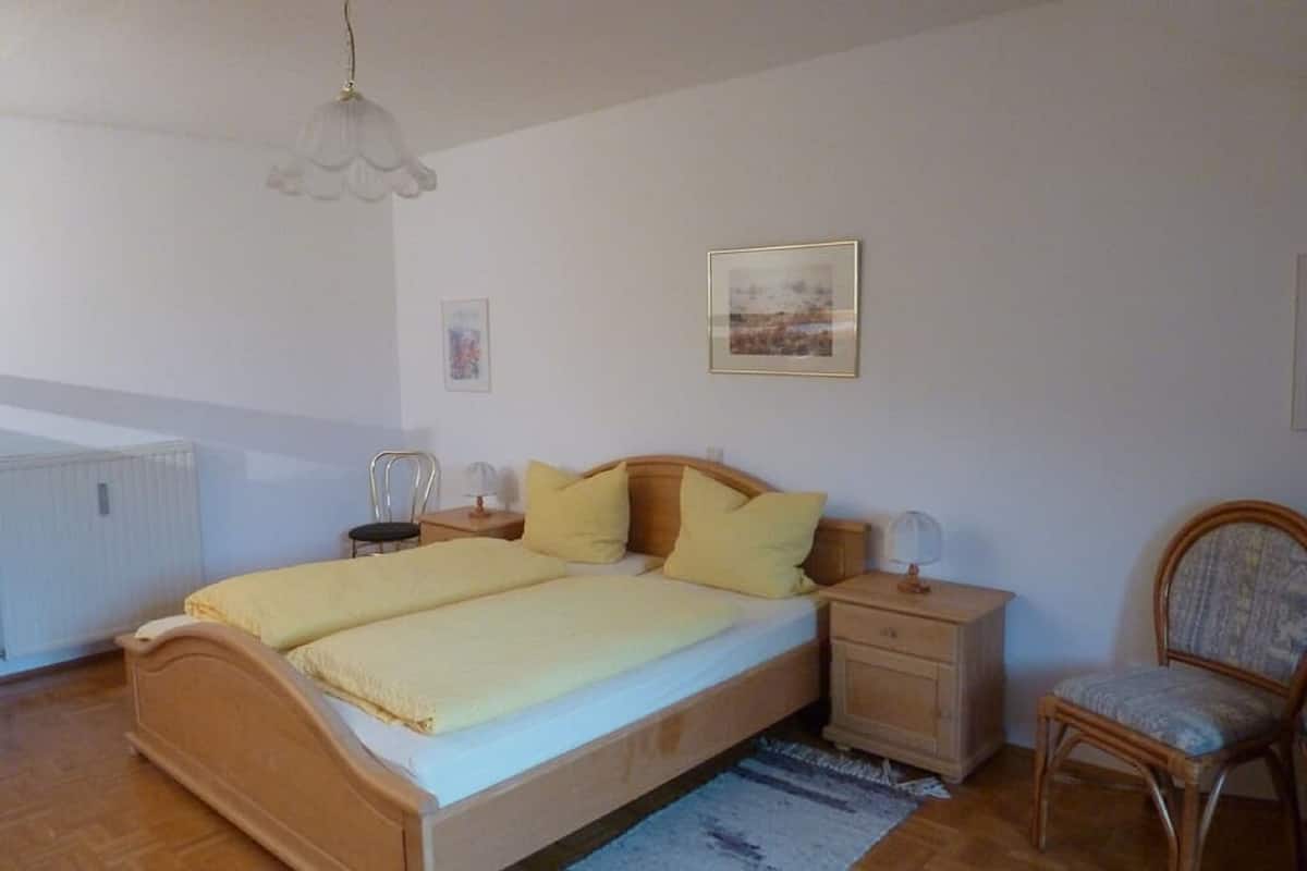 Une chambre à coucher avec un lit en bois, une table de chevet, une chaise, un radiateur et un tableau accroché au mur.