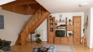 A living room with a wooden staircase, a sofa, a TV, and wooden cabinets. - Appartementhaus Osserblick (Lohberg)