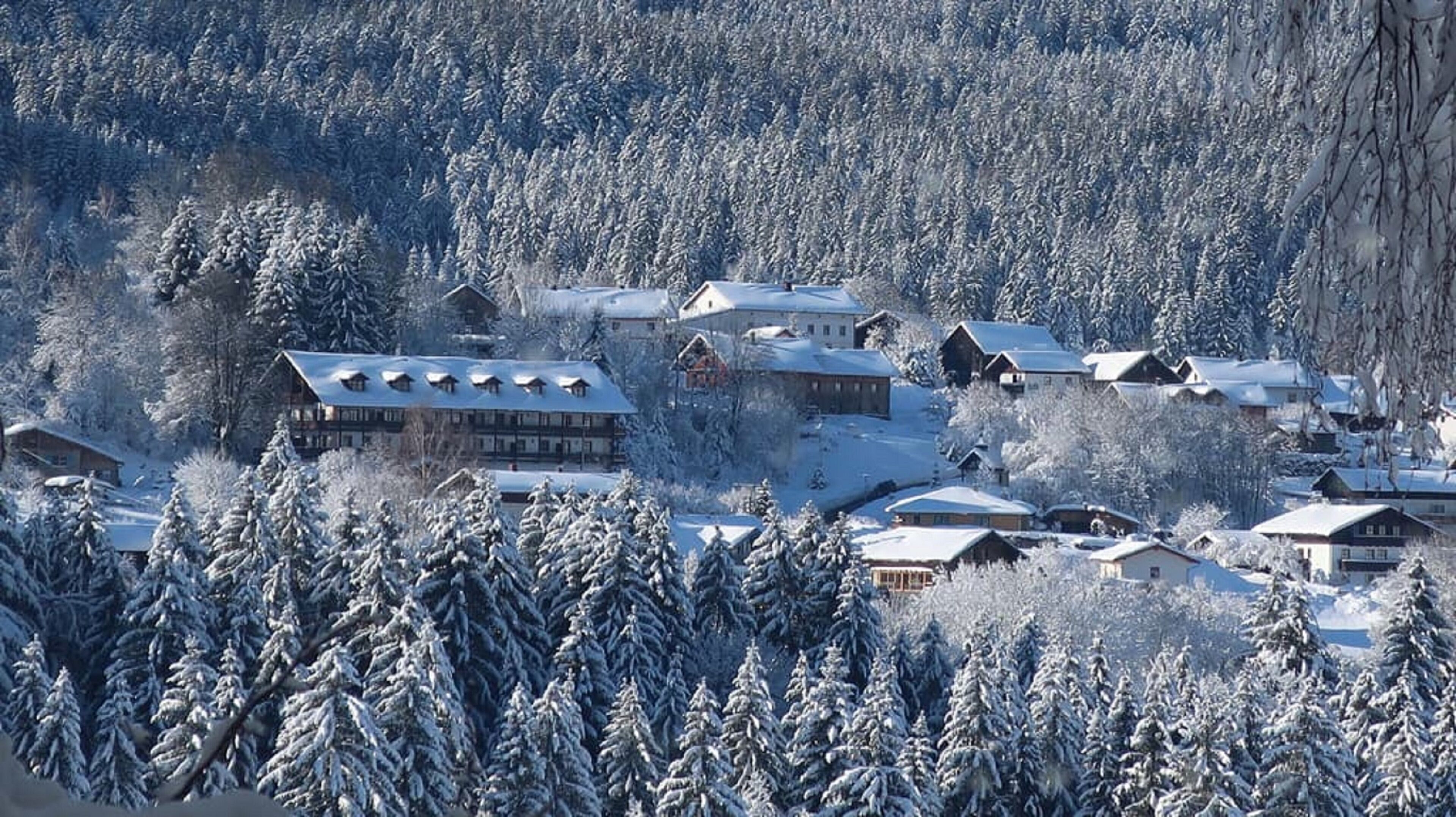 Un pueblo cubierto de nieve con varios edificios, incluyendo un gran alojamiento con un techo destacado y varias casas más pequeñas.