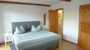A bedroom with a bed, nightstands, a wooden wardrobe, and a bathroom visible through an open door. - Appartementhaus Osserblick (Lohberg)