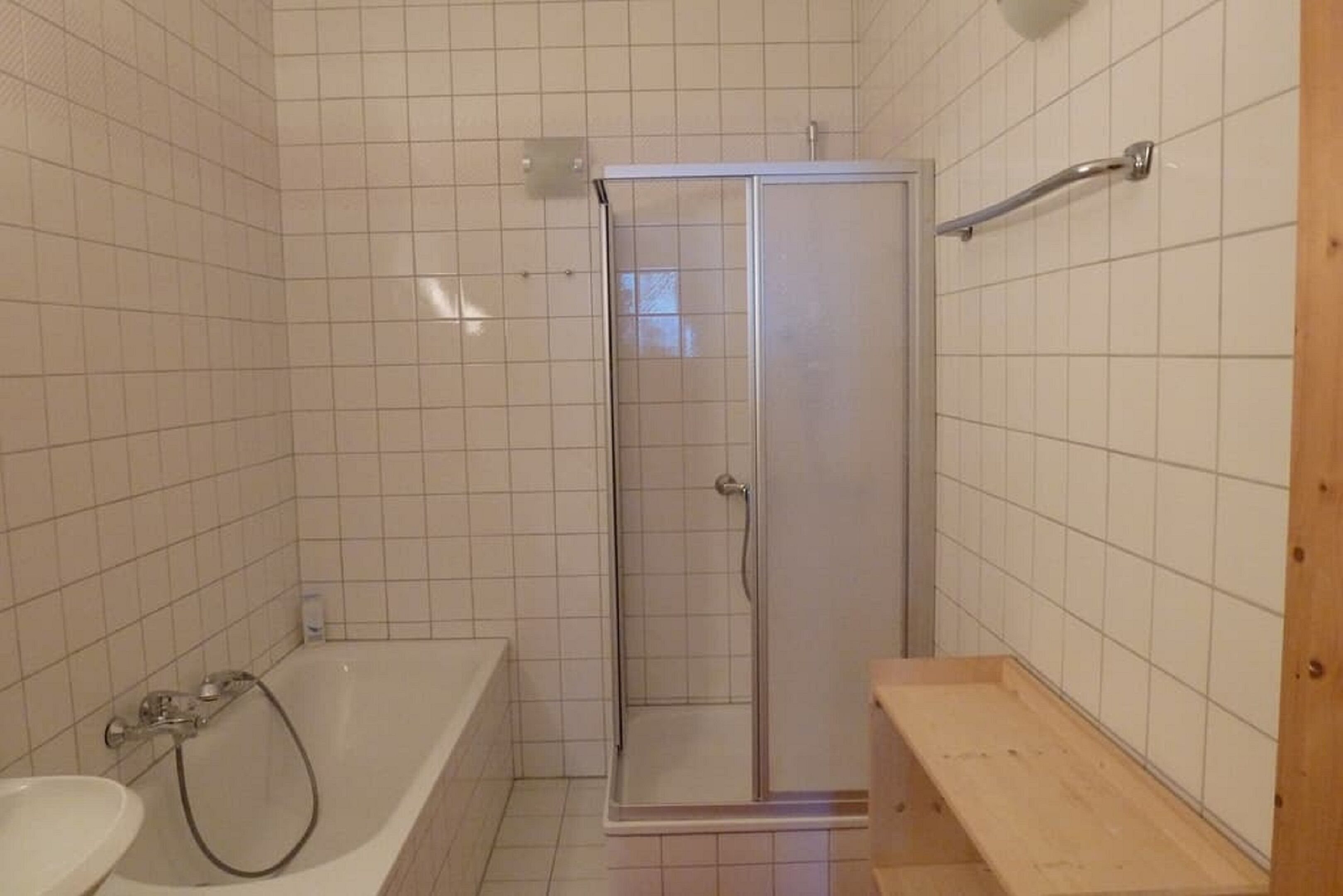 A bathroom with a glass-enclosed shower, a bathtub, and a wooden shelf.