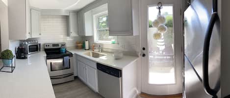 A modern kitchen with white cabinetry, a stainless steel refrigerator, a dishwasher, and a window with a view of the outdoors.
