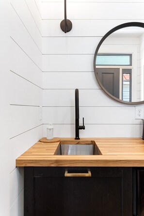 A modern bathroom with a wooden countertop, black cabinet, and a round mirror. - The Sunrise | 3BR Up - Best of Charleston Award! (Charleston)