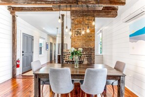 A dining area with a wooden table, grey upholstered chairs, a brick wall, hanging light bulbs, and a fire extinguisher on the wall. - The Sunrise | 3BR Up - Best of Charleston Award! (Charleston)