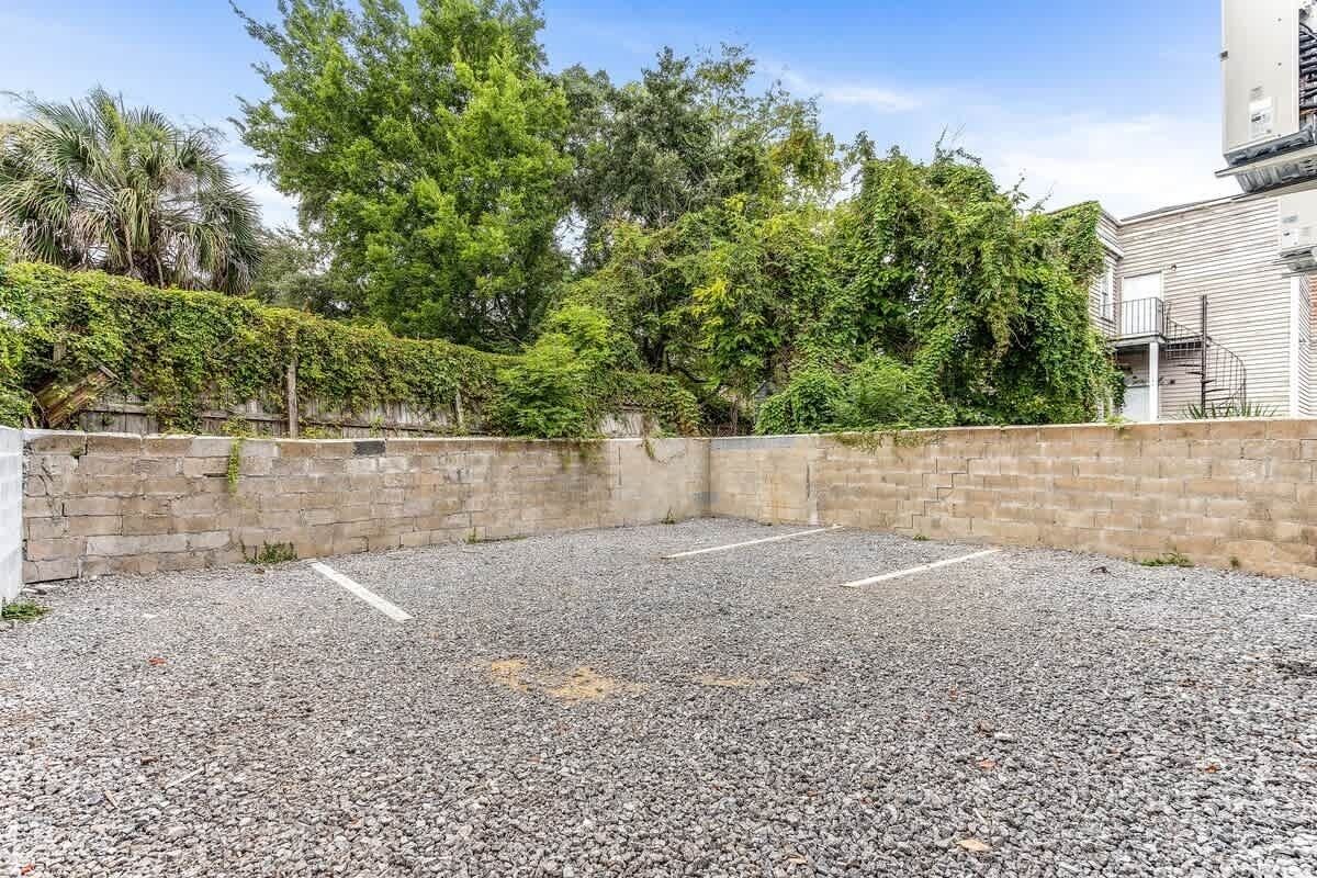 A gravel parking area with a brick wall and trees in the background.