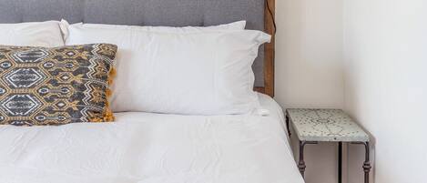 A bedroom with a bed, a bedside table, a wall-mounted light, and a painting.