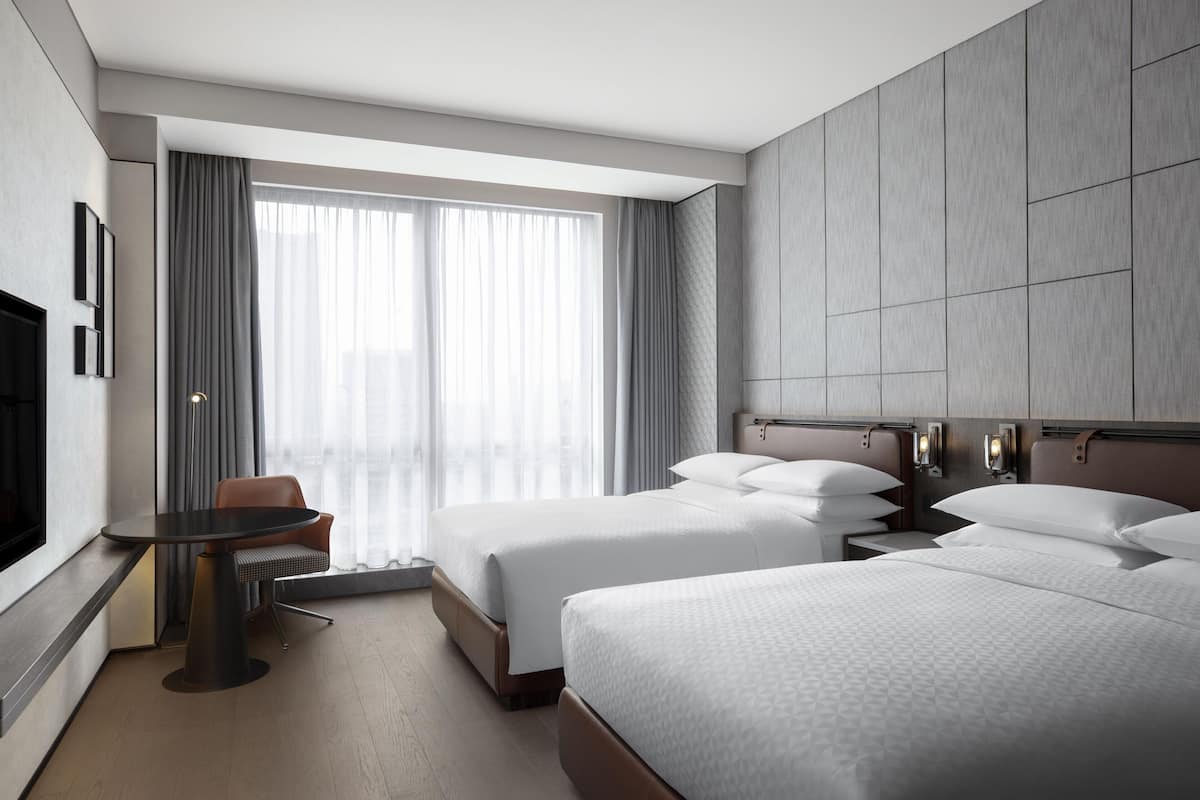 A hotel room with two beds, a desk, and a TV.