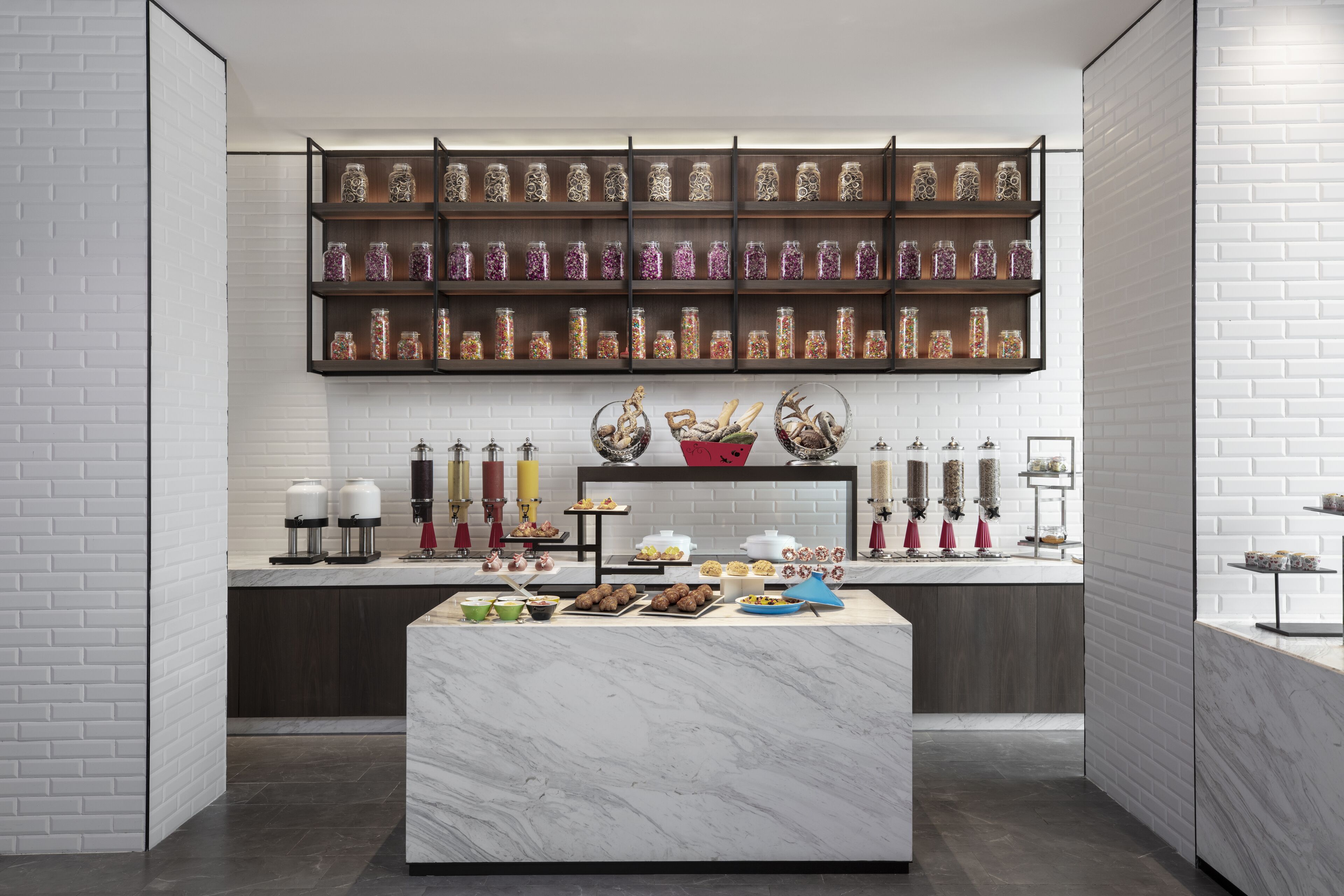 A modern kitchen with a marble island, a coffee station, and shelves with jars of spices.