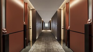 Et hotel med et korridor med et mønstret tæppe, trævægge og en lang gang der fører til en lys ende.
