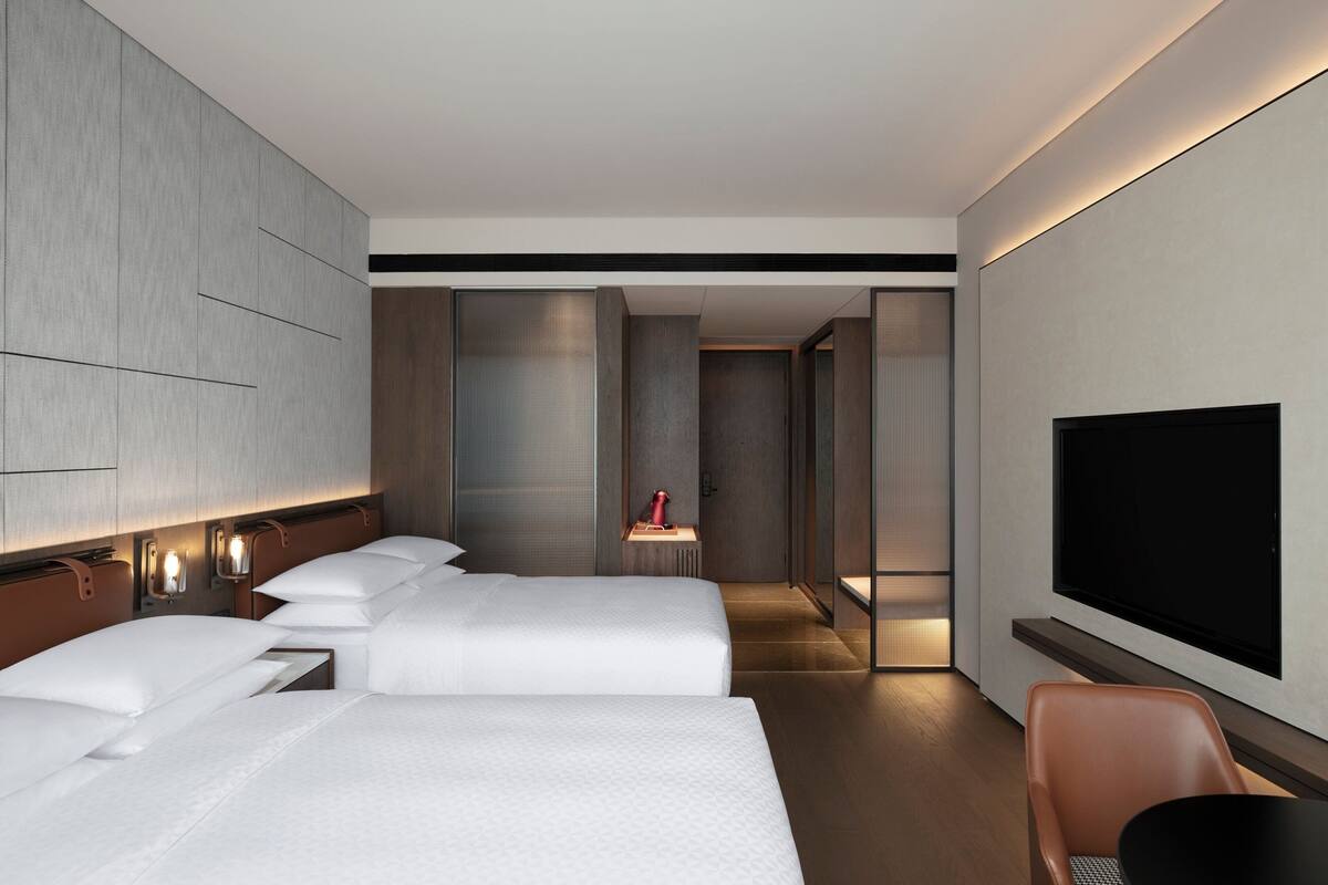 A modern hotel room with two beds, a flat-screen TV, a desk, and a chair.