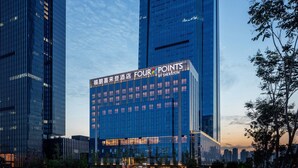 Et højt hotel med et tydeligt 'Four Points by Sheraton' skilt, omgivet af andre høje bygninger og træer.