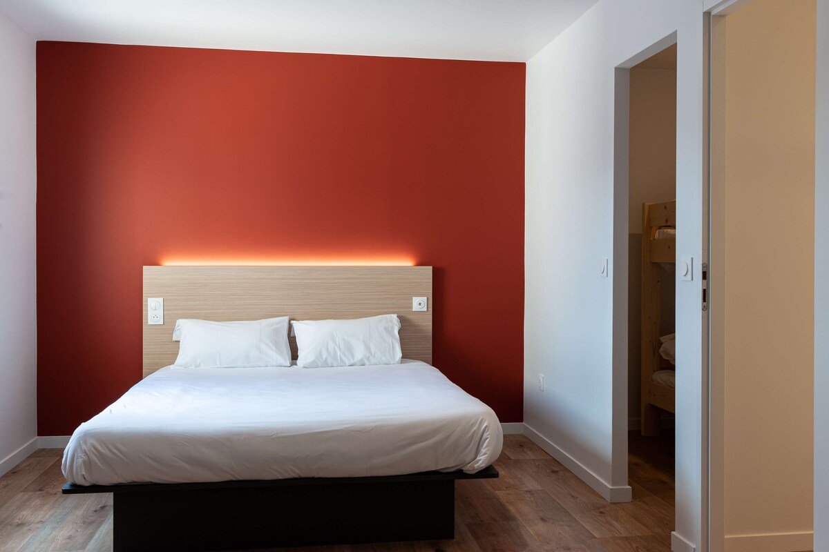 A bedroom with a bed, a red accent wall, and a wooden floor.
