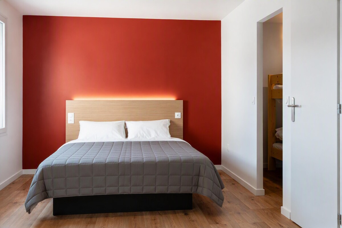 A bedroom with a bed, a red wall, and a wooden floor.