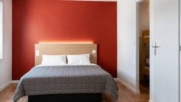 A bedroom with a bed, a red wall, and a wooden floor.