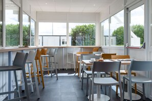 A modern cafe with large windows, white and gray chairs, and a clean, bright interior. - PREMIERE CLASSE BEAUNE (Montagny-les-Beaune)