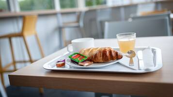 A breakfast tray with croissant, juice, and yogurt on a table with a view of a cityscape.