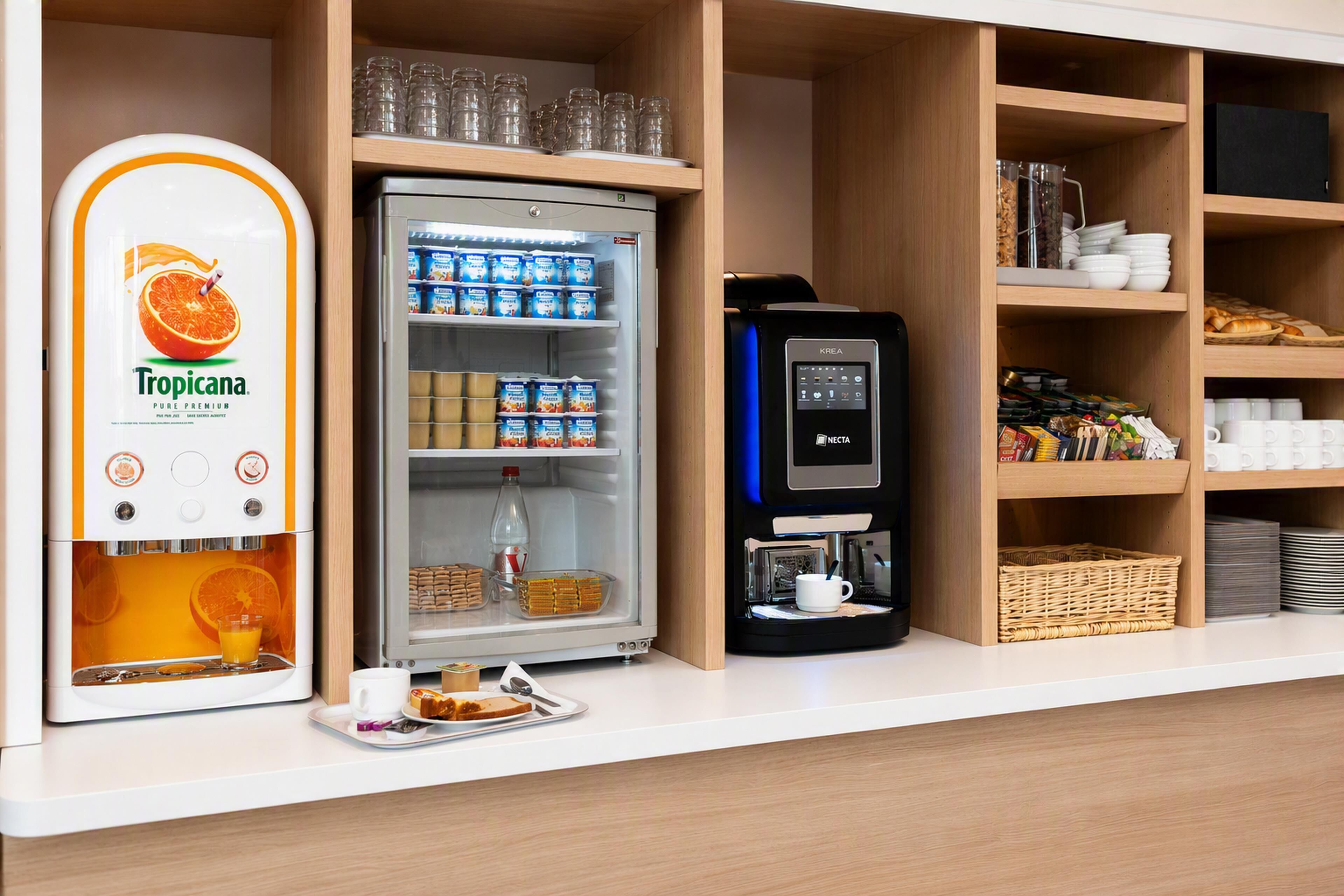 Ett litet kök med en kaffemaskin, ett kylskåp fyllt med drycker och en juiceautomat.