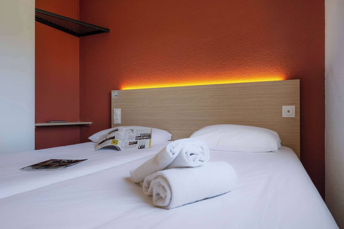 A hotel room with a wooden headboard, white bedding, and a magazine on the bed.