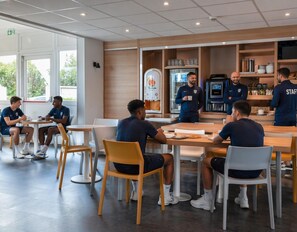 A modern cafe with tables and chairs, a coffee machine, and shelves with items.
