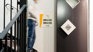 Una persona baja una escalera en un edificio, con un cartel que indica los números de habitación de 300 a 328 y de 200 a 228.