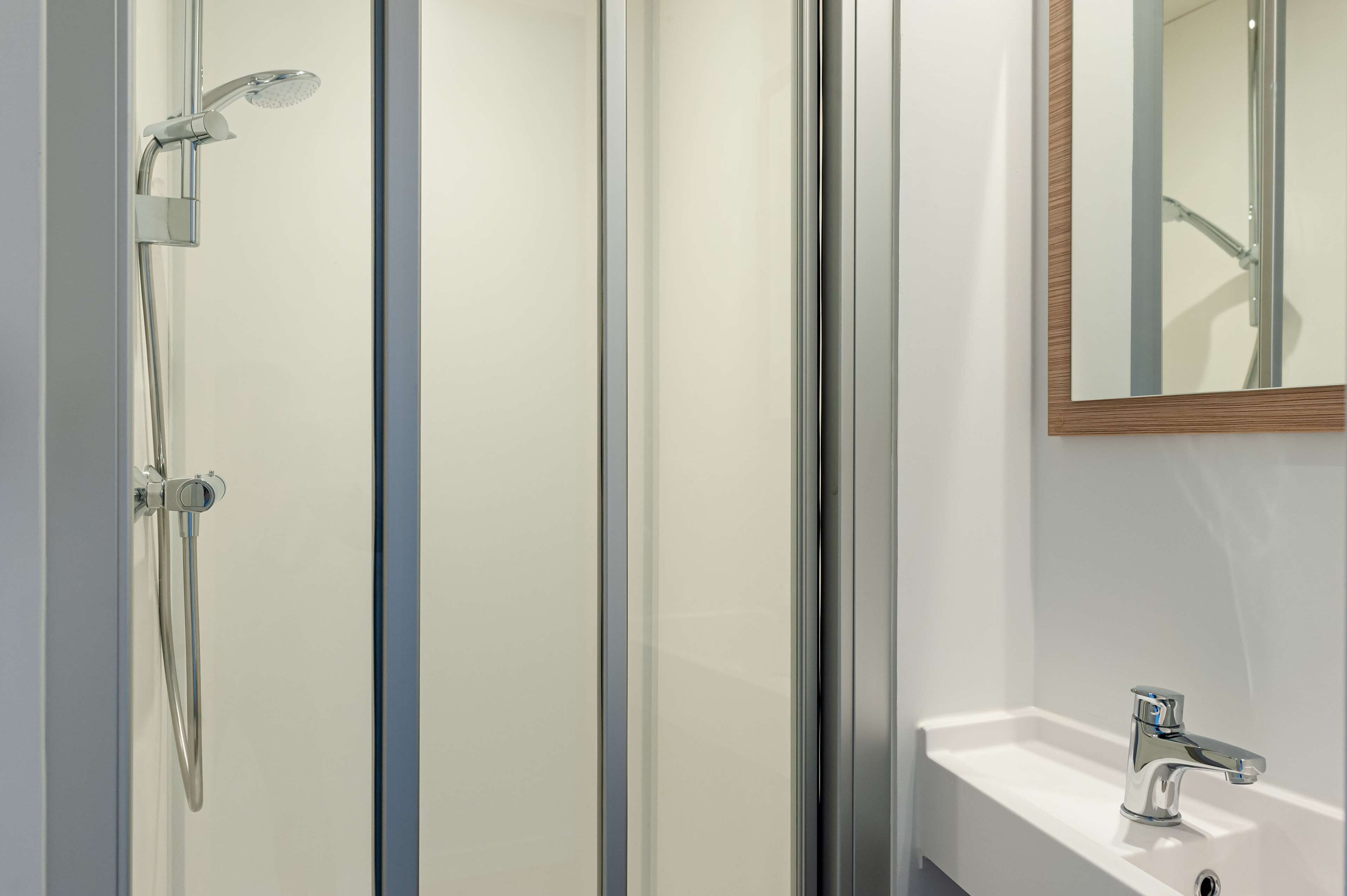 Un bany modern amb una cabina de dutxa de vidre, un lavabo amb un aixeta cromada i un mirall amb marc de fusta.