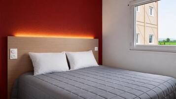 A bed with a headboard, two pillows, and a window with a view of a building.