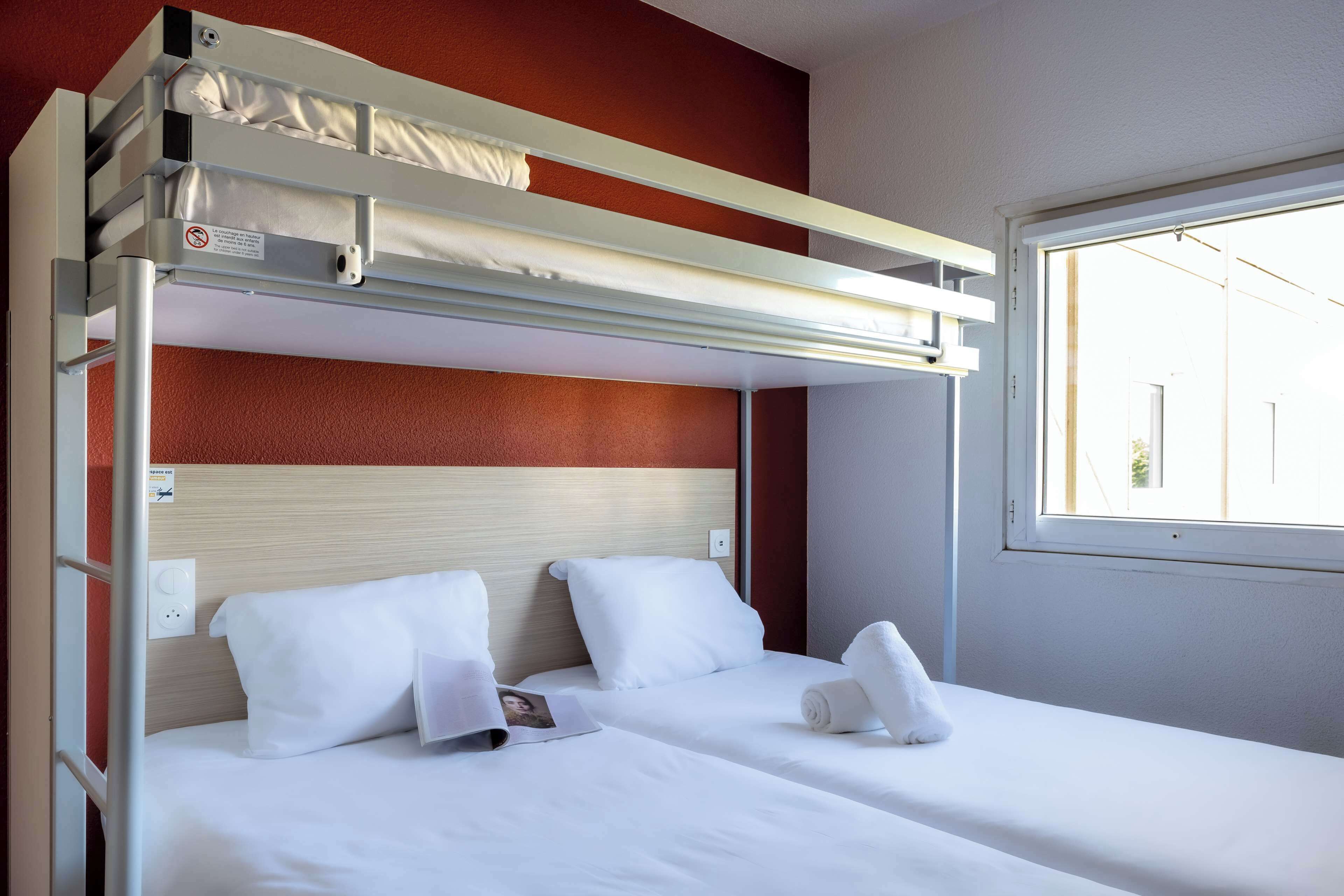A bunk bed with a headboard, white bedding, and a window with a view of buildings.