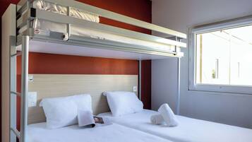 A bunk bed with a headboard, white bedding, and a window with a view of buildings.