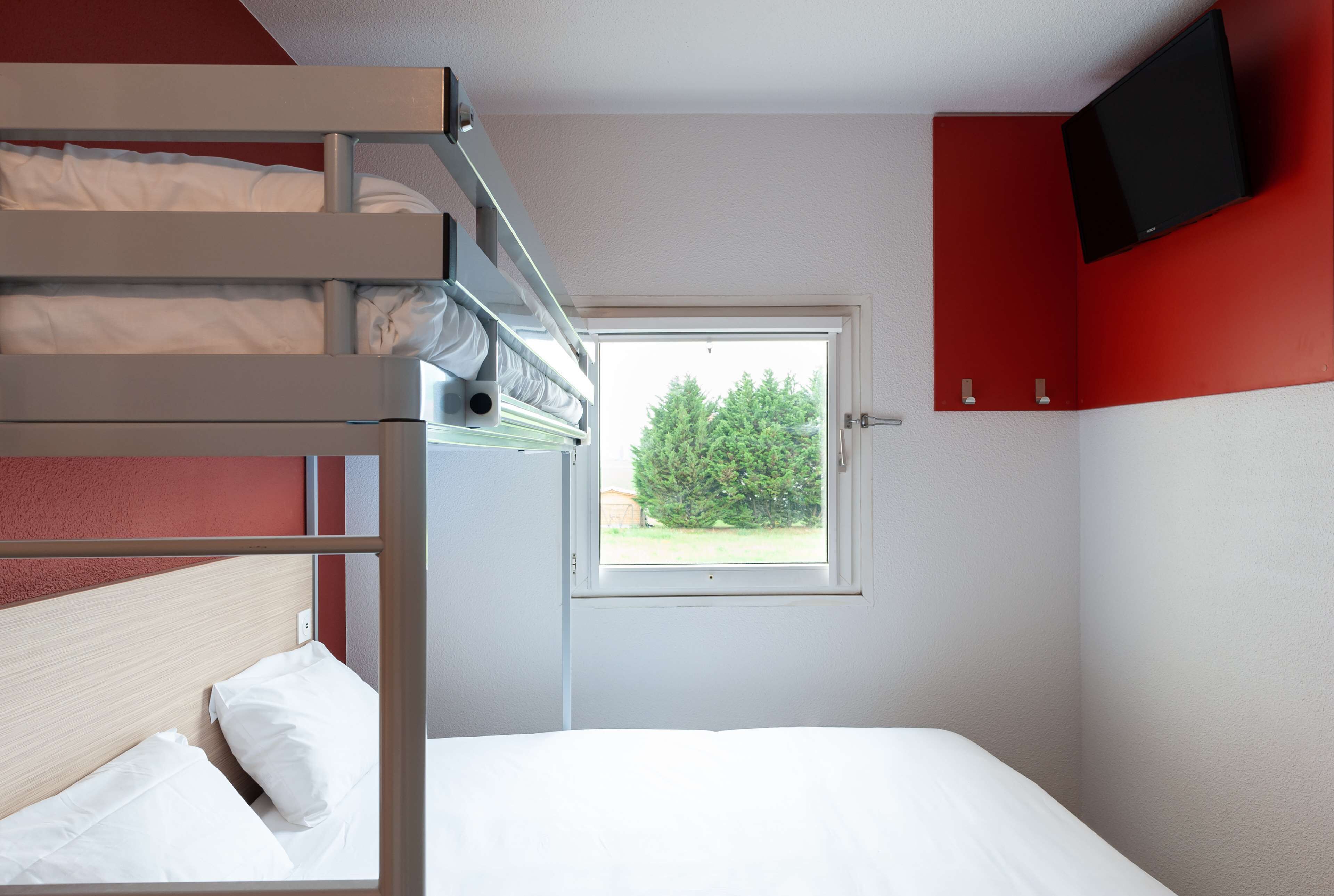 Een slaapkamer met stapelbed, een raam, een aan de muur bevestigde televisie en een rode kast.