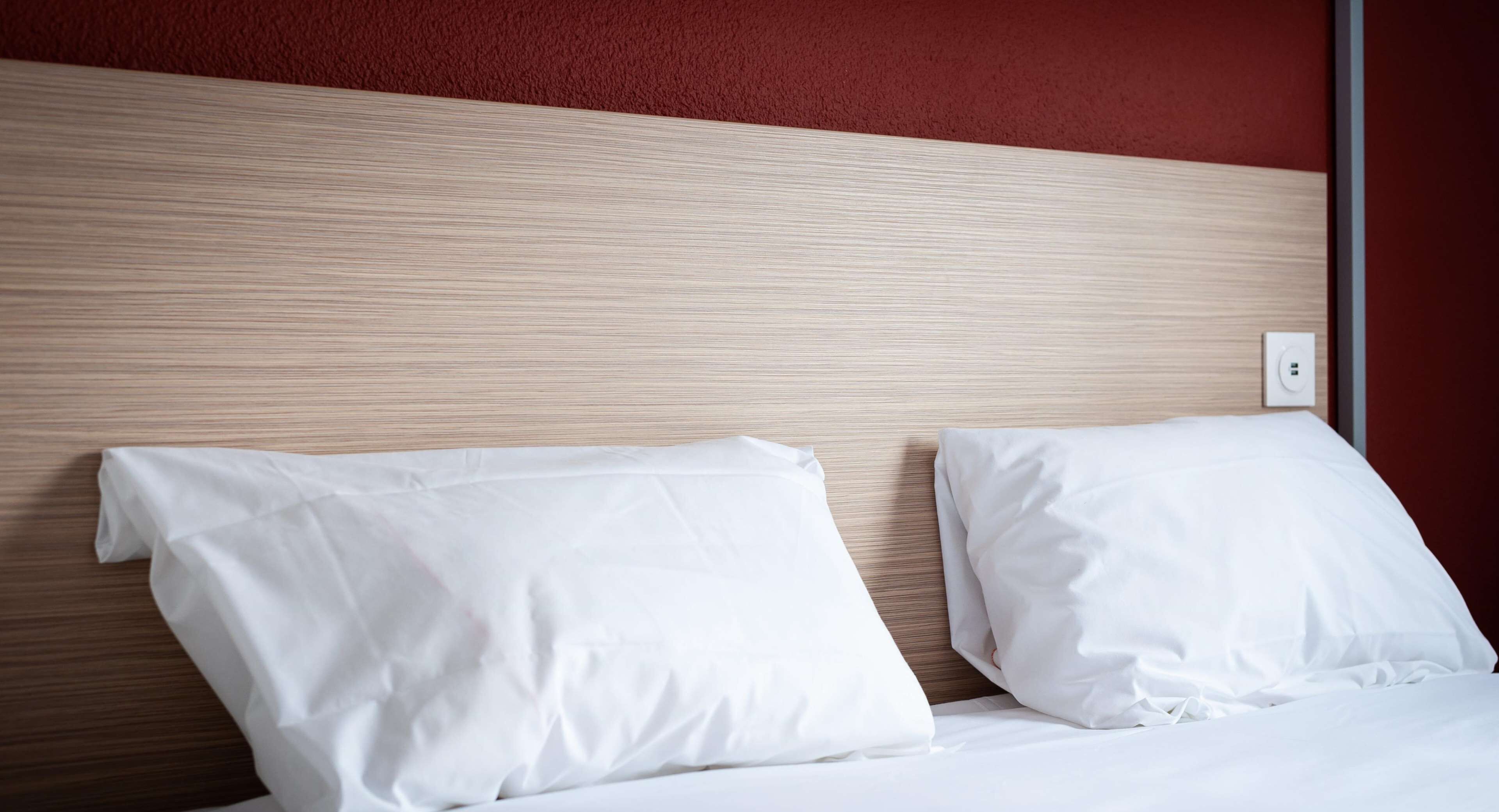 A hotel room with a wooden headboard, two white pillows, and a white bedspread.