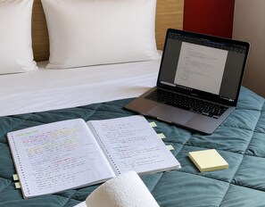 A laptop on a bed with a notebook and sticky notes.