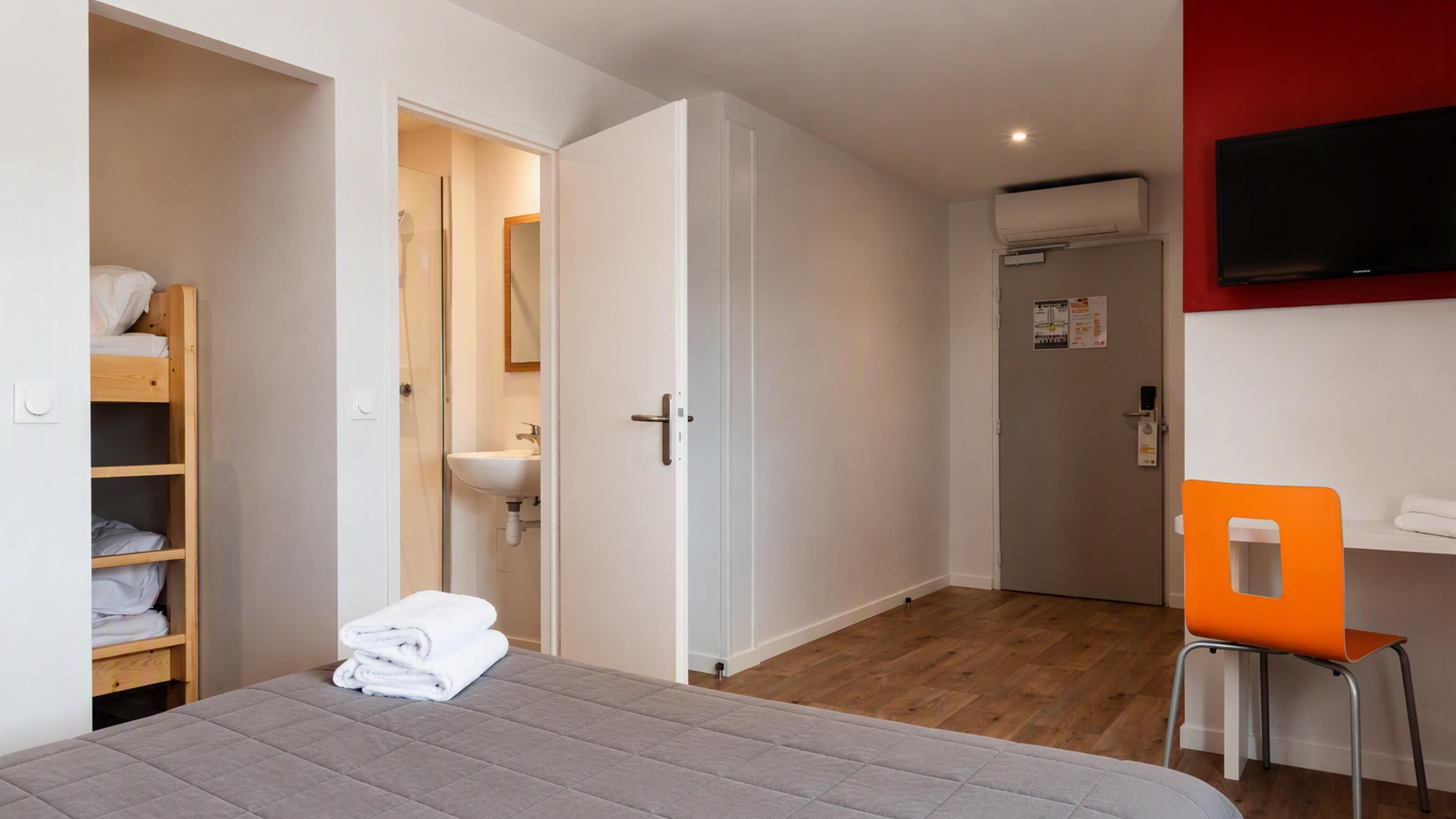 Une chambre d’hôtel comprenant un lit, une armoire en bois, une salle de bain avec un lavabo et un téléviseur fixé au mur.