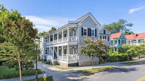 A two-story house with a front porch, a stone foundation, and a red roof. - Six on Cannon | 6BR Charleston Home + Parking (Charleston)