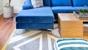 A living room with a blue sofa, a wooden coffee table, and a geometric rug. - Six on Cannon | 6BR Charleston Home + Parking (Charleston)
