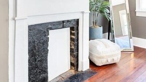 A room with a fireplace, a framed picture of a llama, and a mirror leaning against the wall. - Six on Cannon | 6BR Charleston Home + Parking (Charleston)