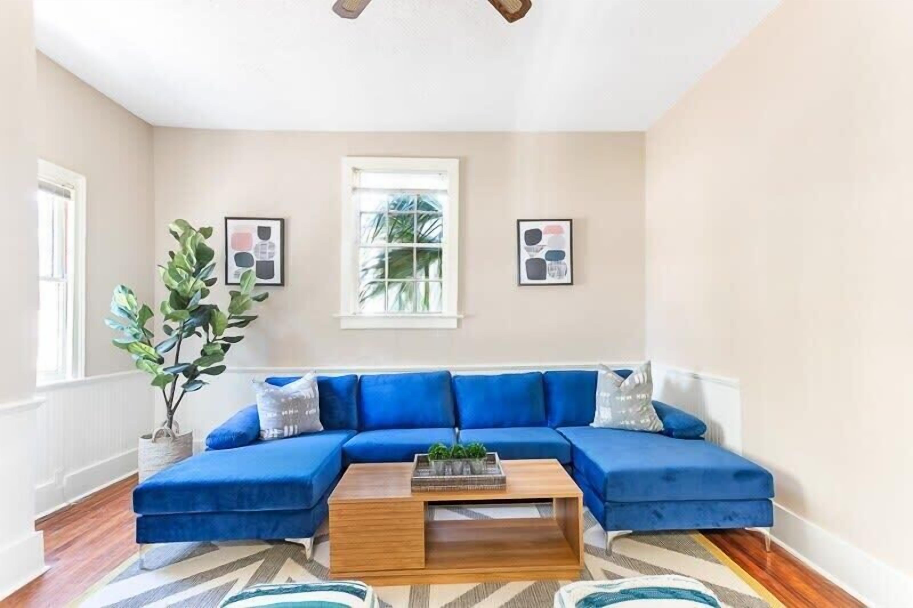 A living room with a blue sectional sofa, a wooden coffee table, and a large window with a view of greenery.