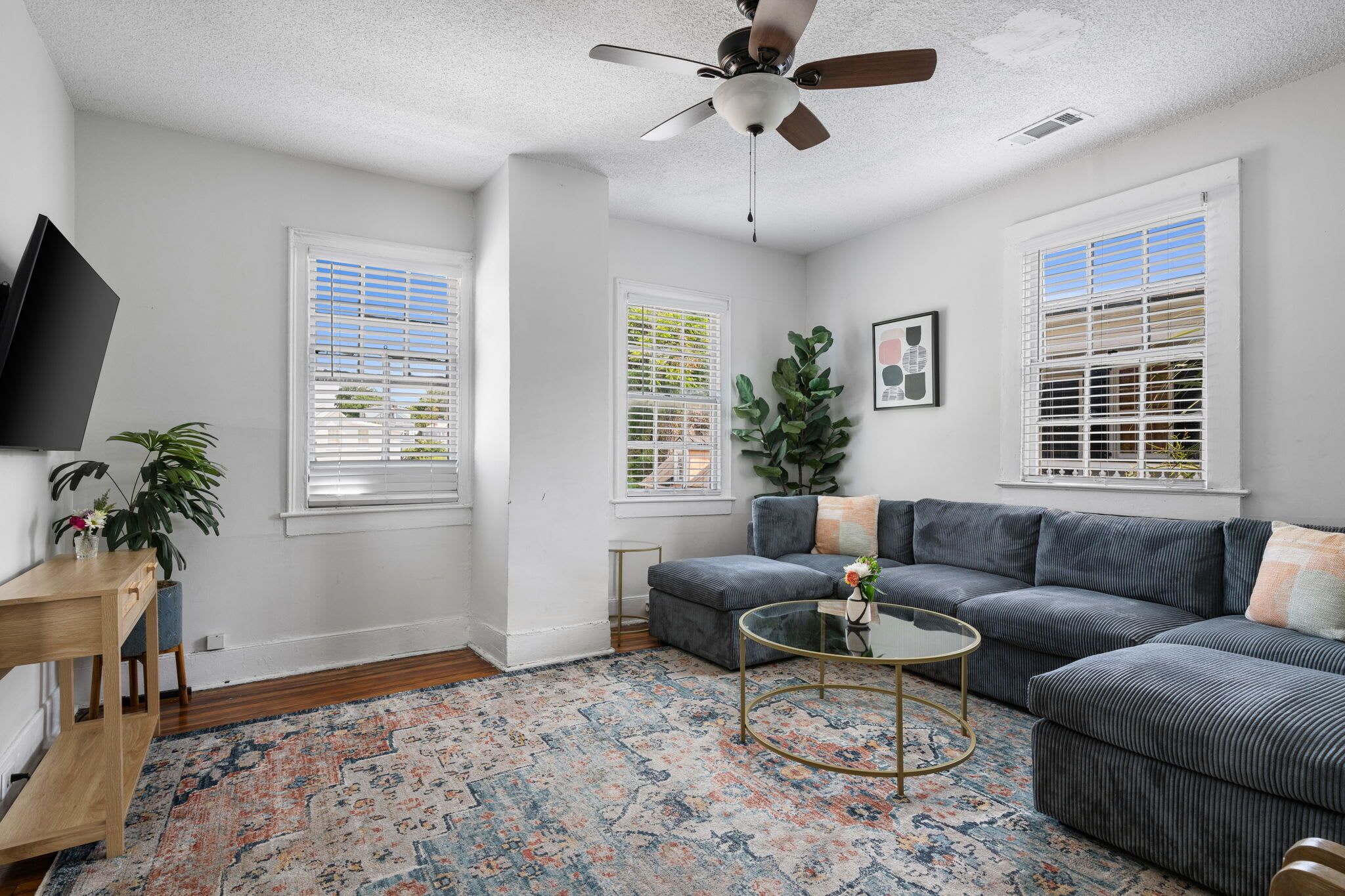 A living room with a gray sectional sofa, a glass coffee table, a wooden side table, and a patterned rug.