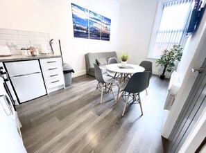 Moderni keittiö, jossa on valkoiset kaapit, harmaa työtaso sekä ruokailutila, jossa on pyöreä pöytä ja harmaat tuolit.