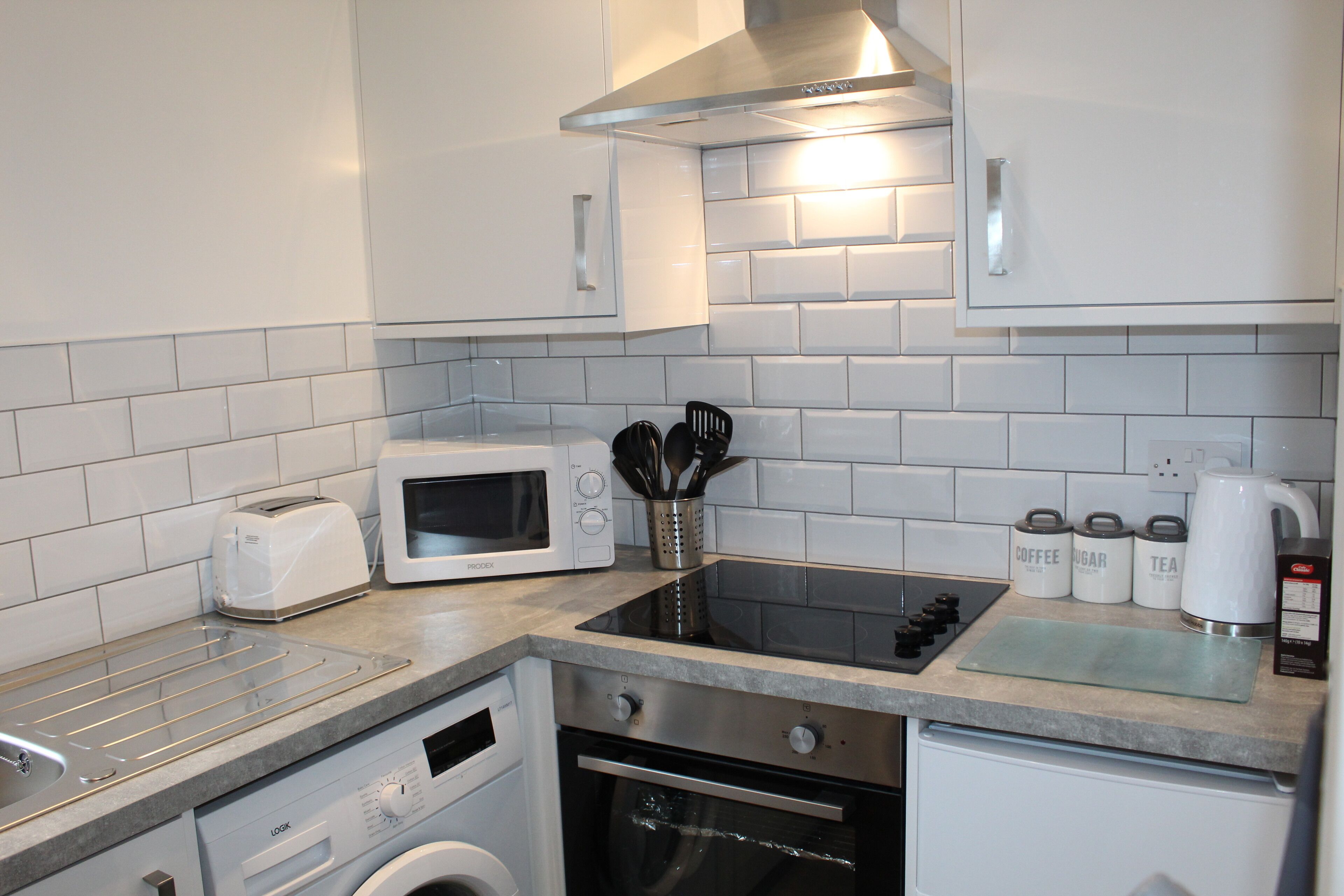 Une cuisine moderne avec des meubles blancs, un four à micro-ondes encastré, une cuisinière et un lave-vaisselle.